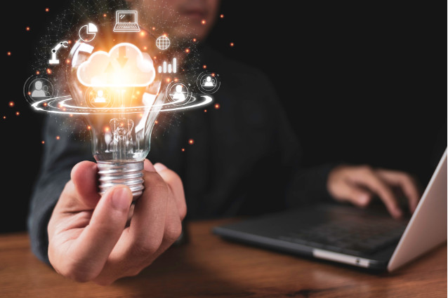 Un homme attablé à son bureau avec son ordinateur portable tient une ampoule dans sa main entourée d'une illustration d'icônes pour symboliser des solutions au référencement.